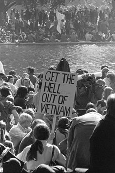 a group of people standing in front of a body of water with a sign that reads get the hell out of vietnam