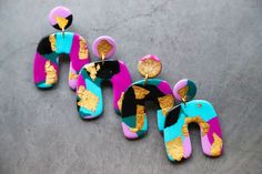 three pairs of colorful earrings with gold and black designs on them sitting on a table