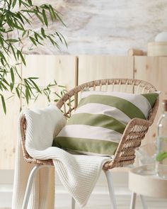 a wicker chair with a green and white striped pillow on top of it next to a table