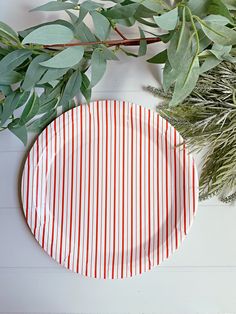 a red and white striped paper plate next to green leaves on a table with greenery