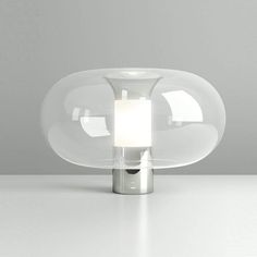 a glass table lamp with a white light on the top and bottom, in front of a gray background