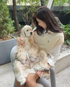 a woman sitting on a bench holding two puppies in her lap and looking at the camera