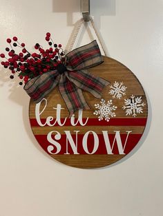 a wooden sign that says let it snow hanging on a wall with some red berries