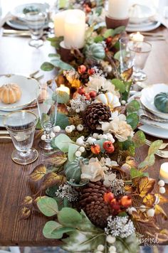 a table is set with candles, plates and pine cones on top of the centerpieces