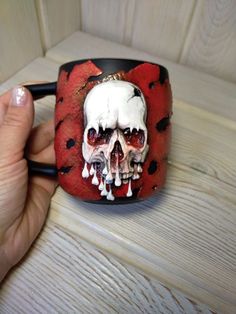 a hand holding a red and black coffee cup with a skull painted on the inside