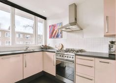 a kitchen with white cabinets and black counter tops, an oven and stove hood in front of large windows