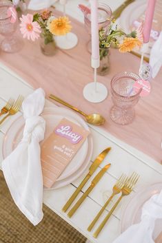 the table is set with pink and white plates, goldware, and napkins