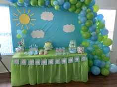 a table topped with balloons and cake next to a wall covered in blue and green balloons