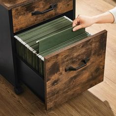 a person is opening a file cabinet with files in it on the floor next to a desk