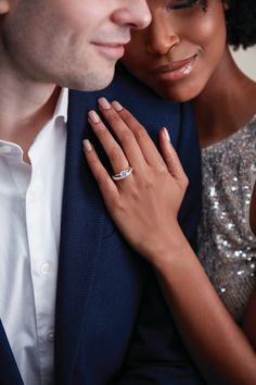 a man and woman embracing each other with their hands on their chest, both wearing wedding rings