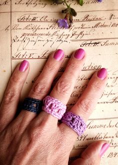 a woman's hand with two crocheted rings on it and flowers in the background