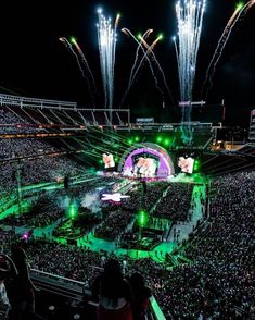 a large crowd at a concert with fireworks in the sky