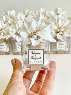 a hand holding a small glass bottle with flowers in it and labels on the bottles