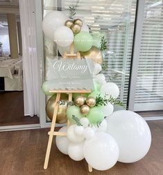 a table topped with balloons and an easer filled with white and gold balloons, greenery and a sign that says whimy