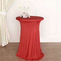 a round table with a red cloth draped over it and white flowers on the top