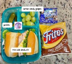 a plastic container filled with food next to a bag of chips and grapes on top of a counter