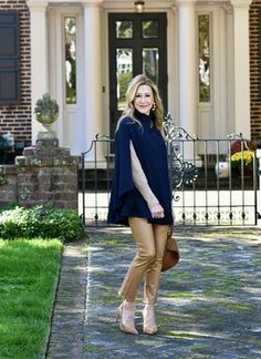 a woman standing in front of a house wearing tan pants and a blue ponchy