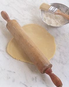 a wooden rolling pin sitting on top of a counter next to a bowl and measuring spoon