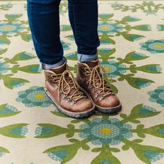 a person wearing brown boots and jeans standing on a floral pattern floor with their feet in the air