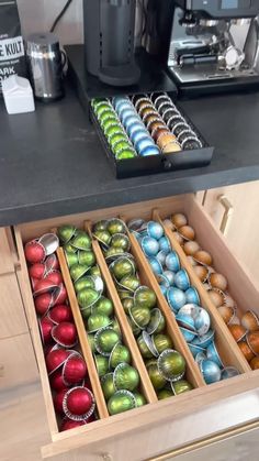 an open drawer filled with lots of different colored balls and tinsels in front of a coffee maker