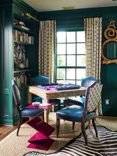 a dining room with green walls and blue upholstered chairs around a wooden table