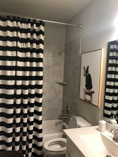 a bathroom with a black and white shower curtain next to a sink, toilet and bathtub