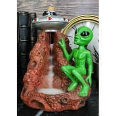 a green alien figurine sitting on top of a rock next to a clock