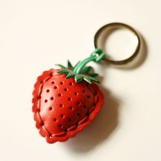 a red leather keychain with a strawberry on the front and green leaves on the back