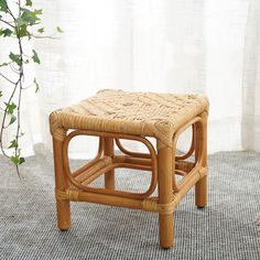 a wicker stool sitting on top of a rug next to a plant in front of a window