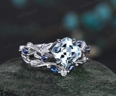 a white gold ring with blue sapphire stones and leaves on it's sides, sitting on top of a rock