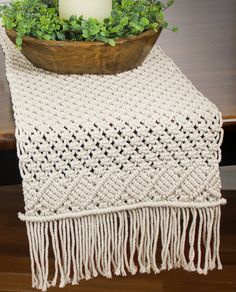 a white table runner with a candle on it and some greenery in a wooden bowl