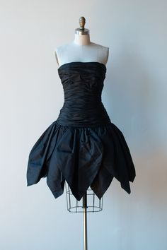 "1980s black petal skirt dress by Victor Costa. 52% nylon 48% polyester. Boning at bodice. Tulle lining at skirt for structure. Plastic zipper, hook & eye and snaps at back. - Size Extra Small - Bust: 32\" - 34\" Waist: 25\" Drop Waist: 36\" Bodice: 16\" Hips: Full Length: 33\" Condition: Excellent!" Waist Drop Dress, Fitted Black Dress With Gathered Skirt, Black Fitted Dress With Gathered Skirt, Fitted Party Dress With Gathered Skirt, Fitted Dress With Gathered Skirt For Party, Black Party Dress With Gathered Skirt, Black Vintage Corset Dress For Formal Occasions, Formal Sleeveless Dress With Gathered Skirt, Pleated Fitted Corset Dress For Evening