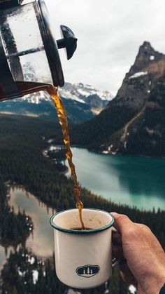 a person is pouring coffee into a cup in front of a mountain lake and snow capped mountains