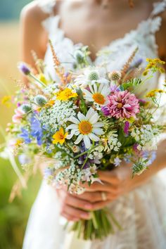 a bride holding a bouquet of wildflowers and daisies in her wedding dress