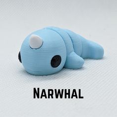 a small blue stuffed animal laying on top of a white surface with the word narwhale written below it