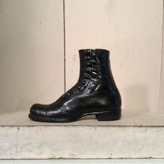 a pair of black leather boots sitting on top of a white shelf next to a wall