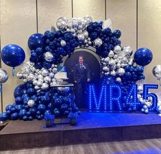 a man standing in front of a blue and silver marquee with balloons on it