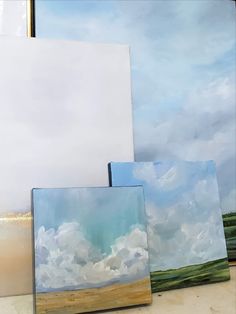 three paintings sitting on top of a table next to each other, one is white and the other is blue