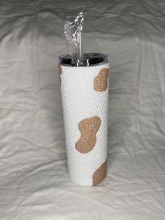 the tumbler cup is decorated with gold polka dots on white paper and has a silver lid