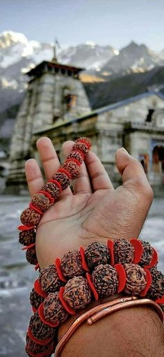 a hand holding some kind of bracelet in front of a building with snow covered mountains behind it