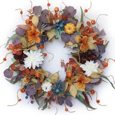 a wreath made out of leaves and flowers on a white background with berries, oranges, and other foliage