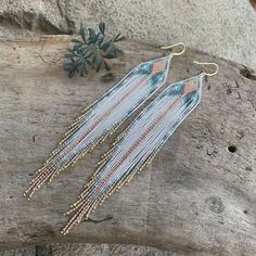 a pair of beaded earrings sitting on top of a piece of wood next to a plant