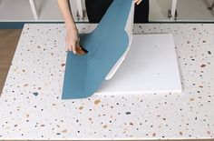 a woman is cutting up a piece of blue paper on a white surface with holes in it