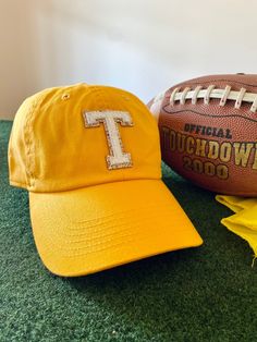 a yellow hat with the letter t on it next to a football