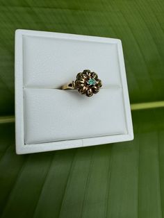 a ring is sitting in a box on a leafy surface with green leaves behind it