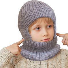 a young boy wearing a gray knitted hat and scarf with his hands on his ears