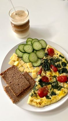 an omelet, bread and cucumbers on a white plate with a drink