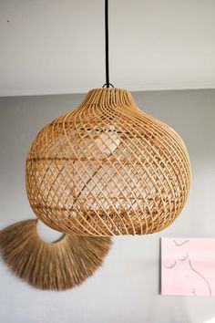 a wicker light fixture hanging from the ceiling in a room with white walls and pink accents