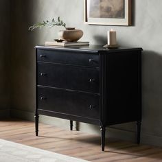 a black dresser with two candles on top of it and a painting in the background