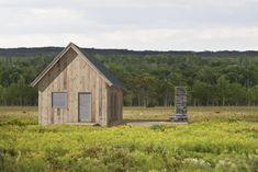 a small wooden building sitting in the middle of a field with tall grass and trees